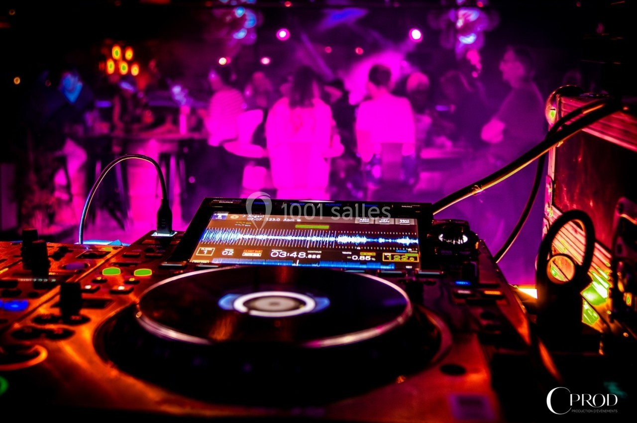 Table de mixage en gros plan dans une ambiance de soirée avec des lumières colorées et des silhouettes en arrière-plan.
