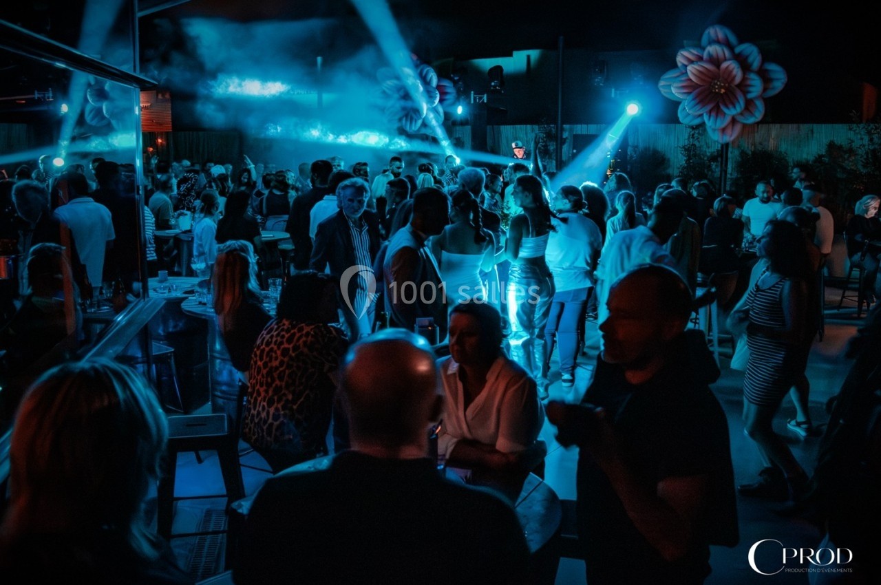 Groupe de personnes rassemblées dans un espace extérieur éclairé par des lumières bleues, ambiance festive.