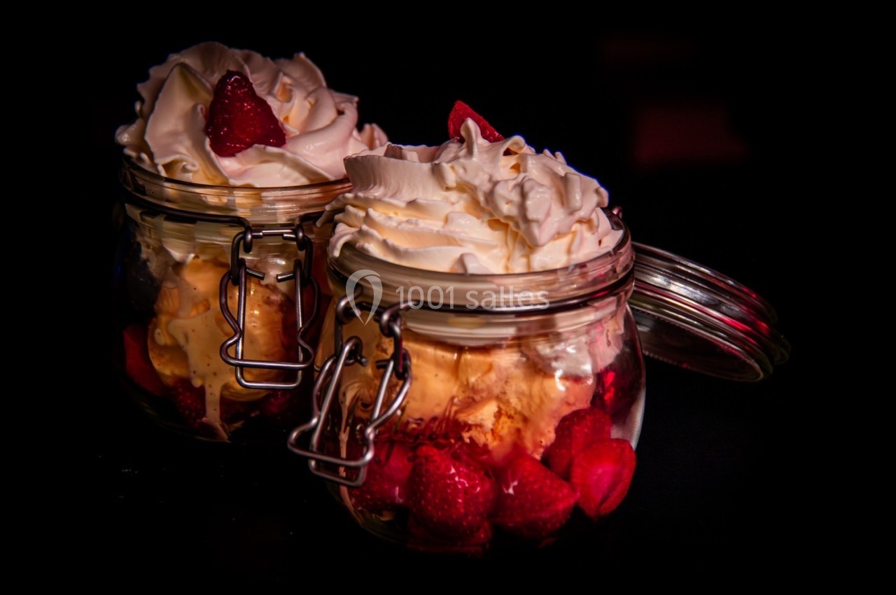 Deux pots en verre remplis de fraises, glace et chantilly, présentés sur un fond sombre.