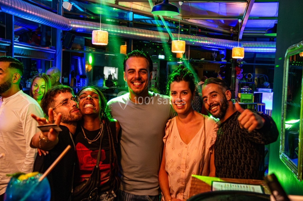 Un groupe de cinq personnes souriantes posant dans un bar animé avec des lumières colorées en arrière-plan.