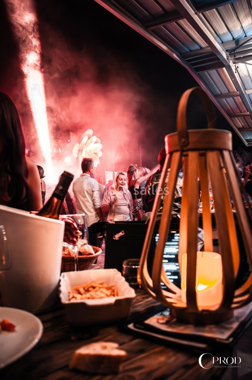 Des convives dans une ambiance festive avec éclairage coloré, vue depuis une table décorée avec une lanterne et des plats.