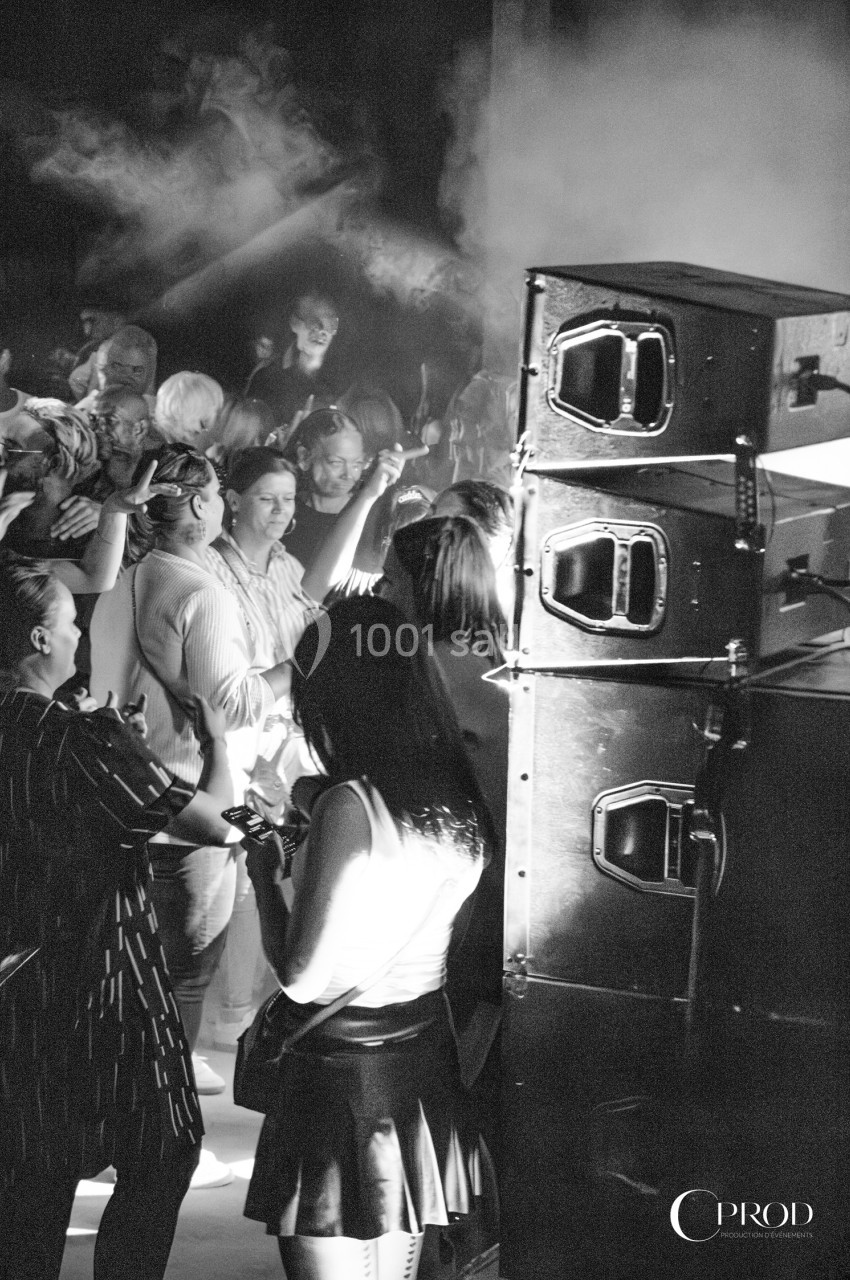 Groupe de personnes rassemblées près d'une enceinte lors d'un événement, éclairées par des lumières tamisées.