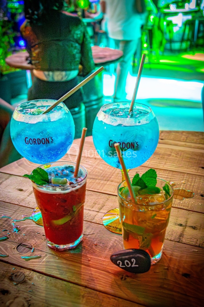 Quatre cocktails colorés sur une table en bois, deux grands verres bleus et deux petits verres avec des garnitures.