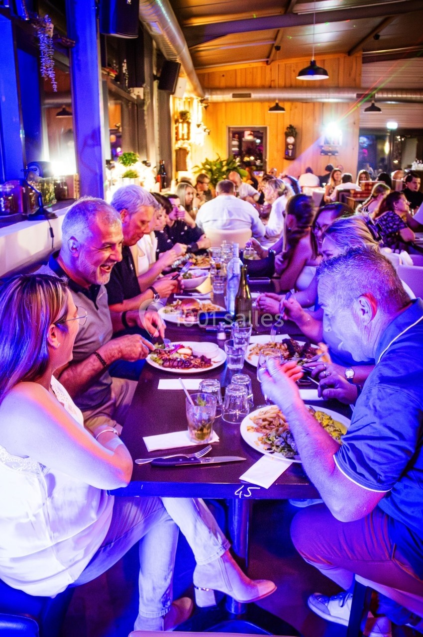Des personnes dînent ensemble dans un restaurant animé, éclairé par des lumières colorées.