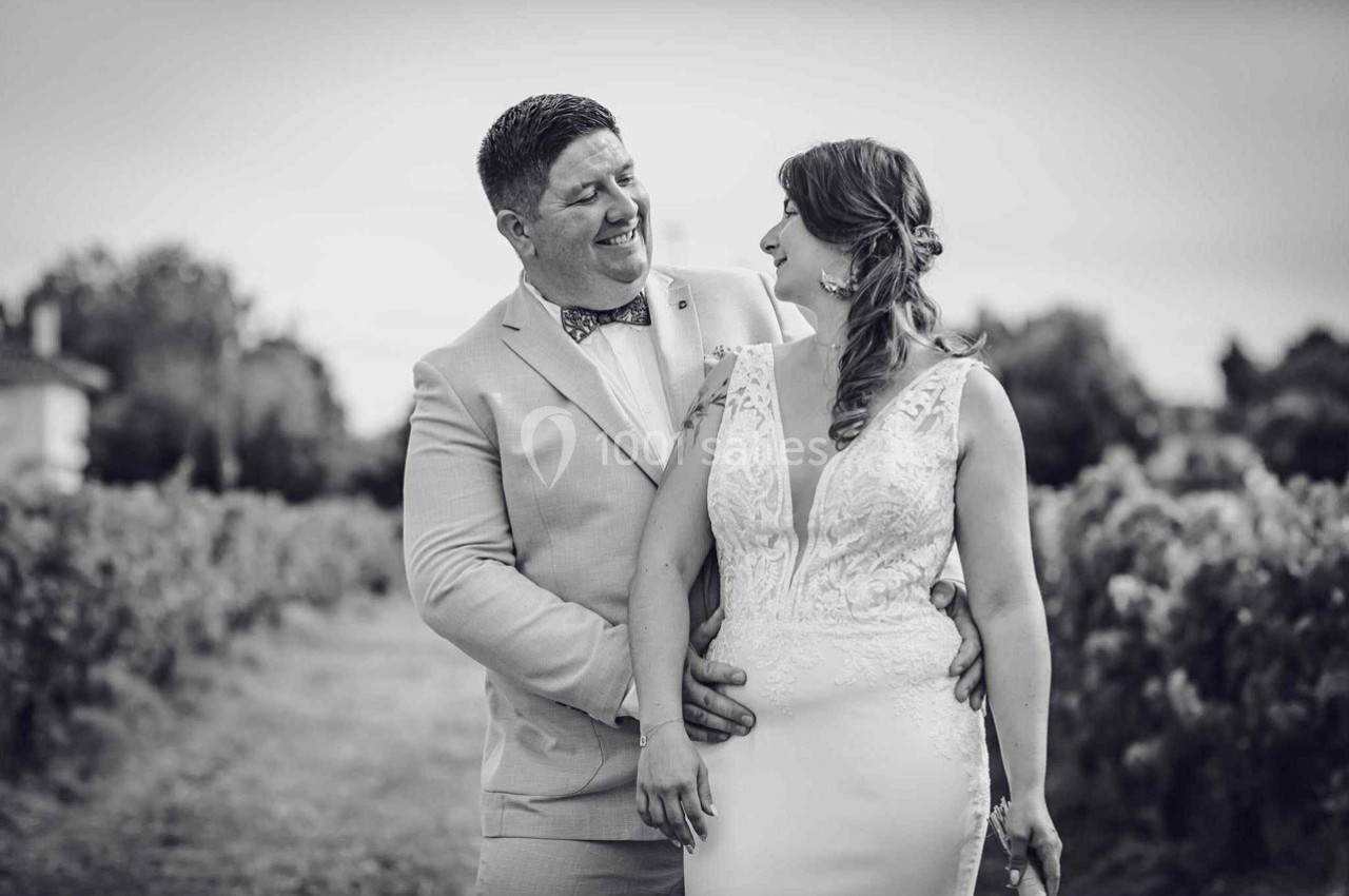 Un couple en tenue de mariage pose dans un vignoble, souriant et regardant l'un vers l'autre.