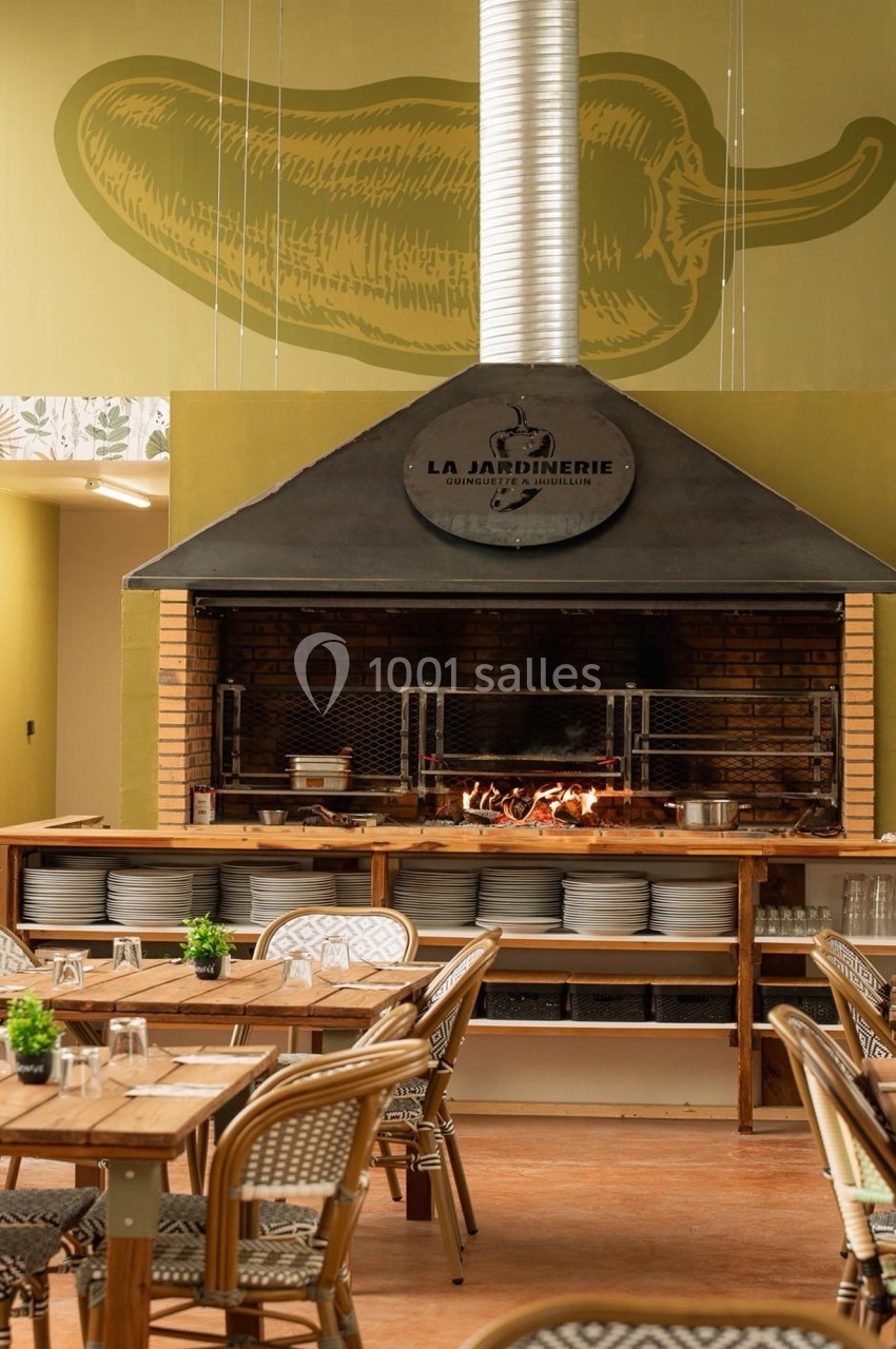 Grill ouvert dans un restaurant, avec tables en rotin, vaisselle rangée et un dessin de piment sur le mur.