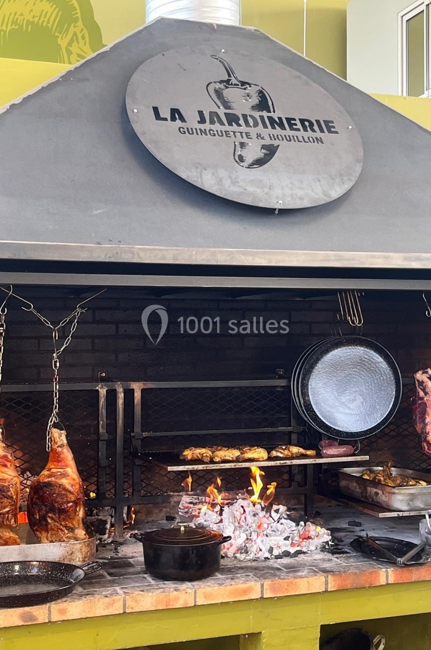 Grillades et viandes suspendues en cuisson sur un barbecue ouvert dans un restaurant nommé ’La Jardinerie’.