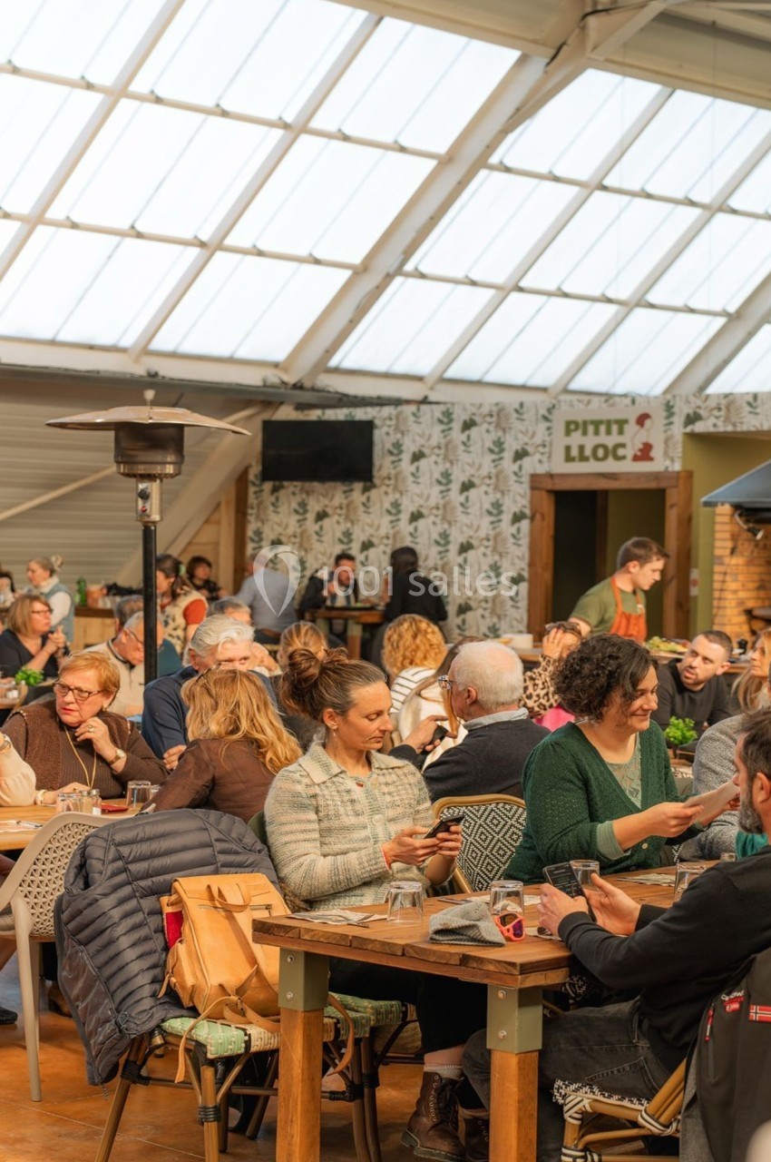 Des personnes assises à des tables dans un restaurant lumineux avec un toit en verre, discutant et partageant un repas.