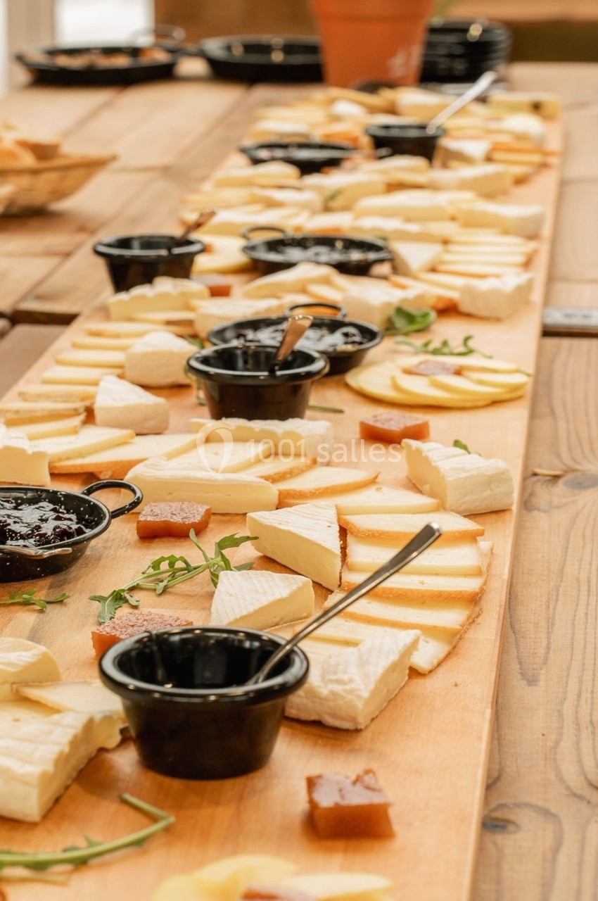 Plateau en bois garni de fromages variés, confitures en coupelles noires et quelques herbes en décoration.