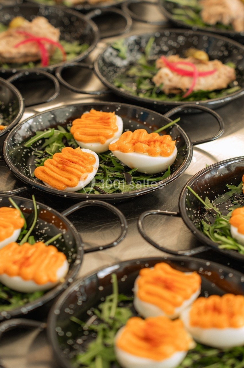 Œufs farcis au jaune d'œuf et sauce orange, présentés sur des assiettes noires garnies de roquette.