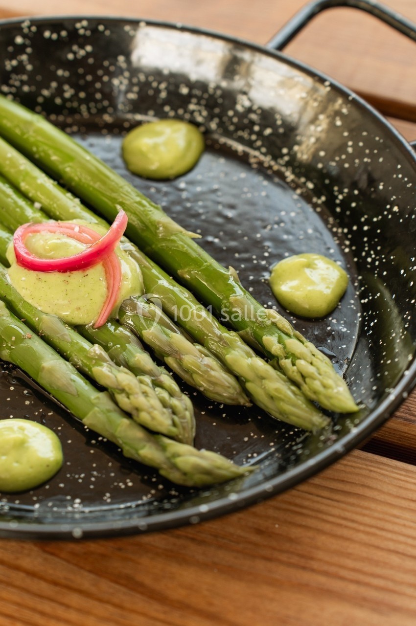 Asperges vertes servies avec une sauce verte et des oignons marinés dans une poêle noire.