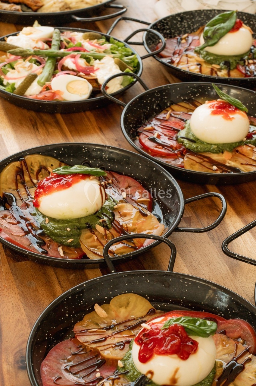 Assiettes de burrata avec tomates, basilic, réduction balsamique et garnitures variées sur une table en bois.