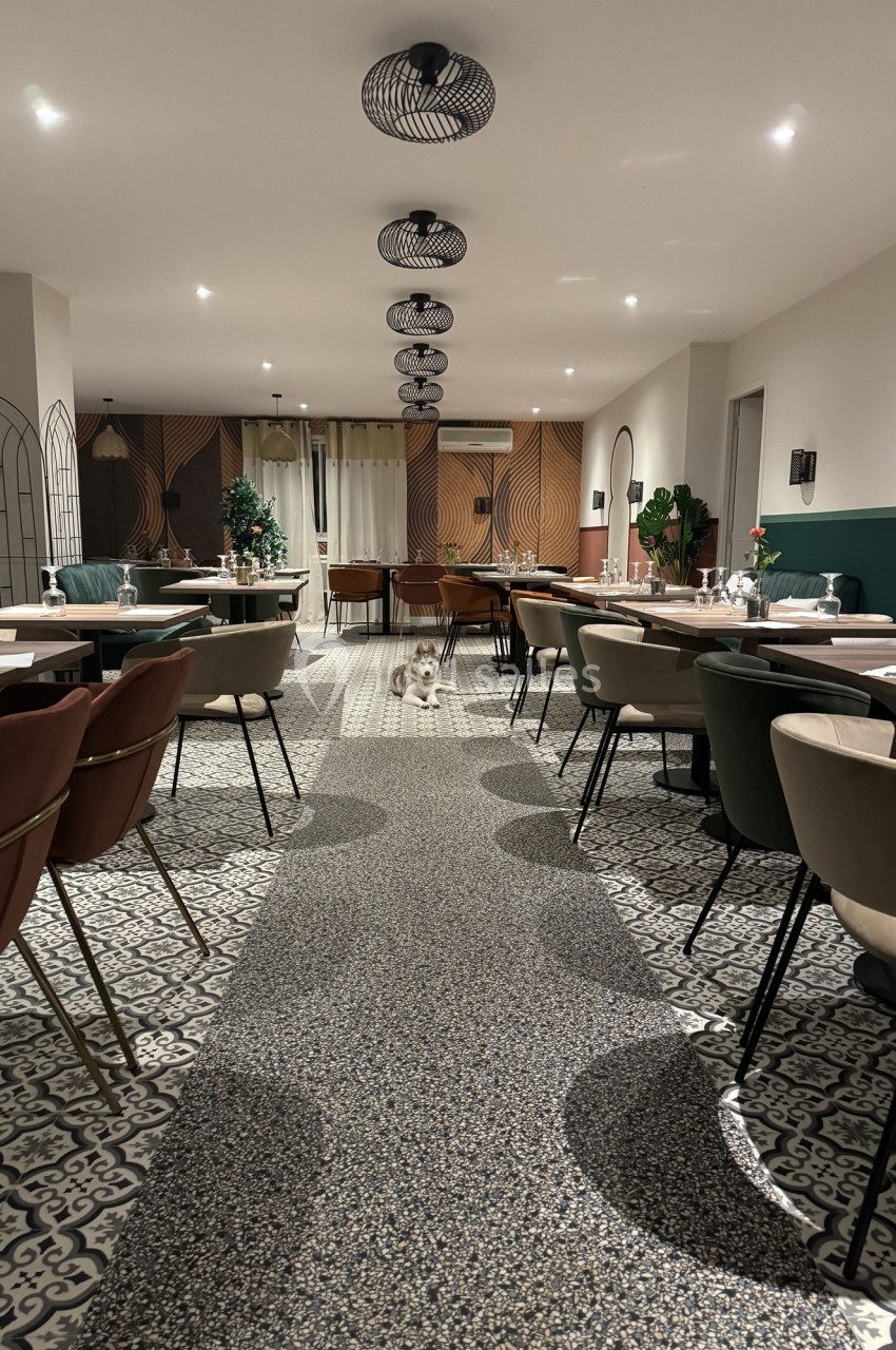 Salle de restaurant moderne avec tables dressées, chaises variées et éclairage suspendu dans une ambiance chaleureuse.