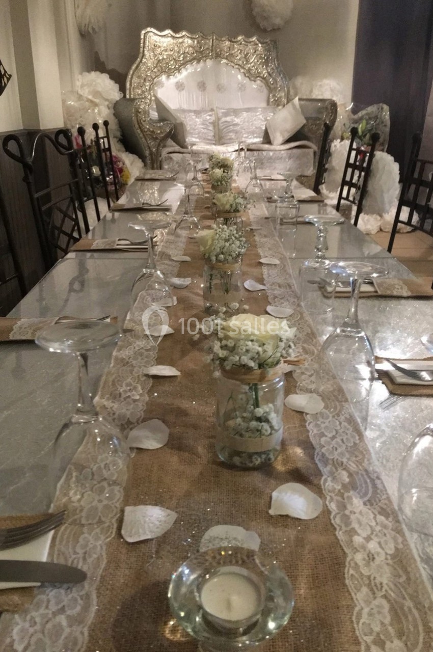 Table décorée pour un événement avec nappe en toile de jute, fleurs blanches, bougies et chaises alignées.