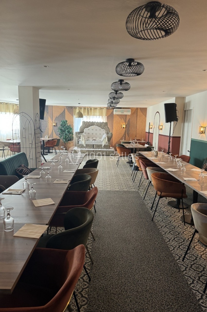 Salle de réception aménagée avec de longues tables dressées, des chaises colorées et un canapé décoratif au fond.