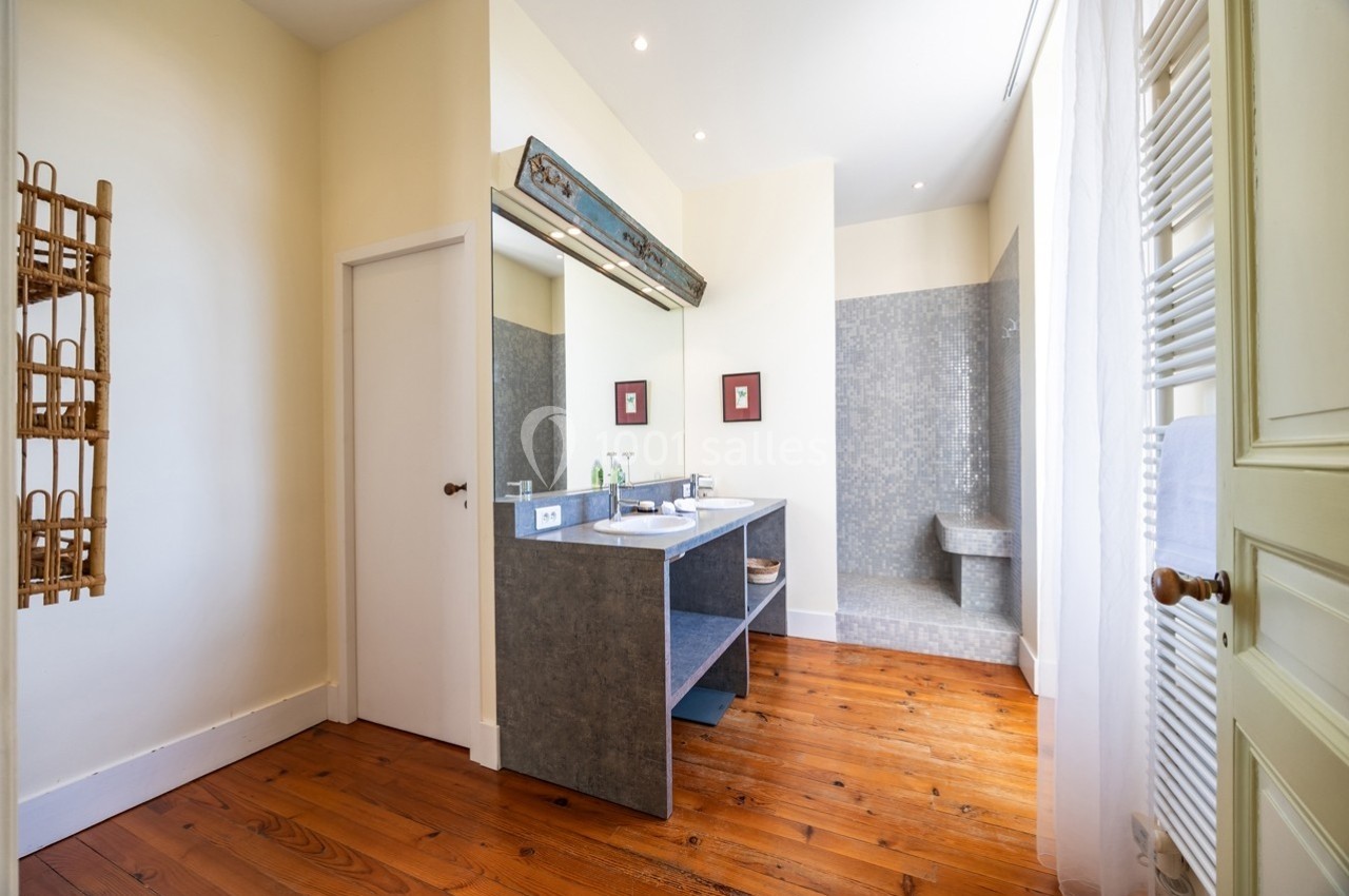 Salle de bain lumineuse avec parquet en bois, meuble vasque gris, douche carrelée et décoration murale minimaliste.