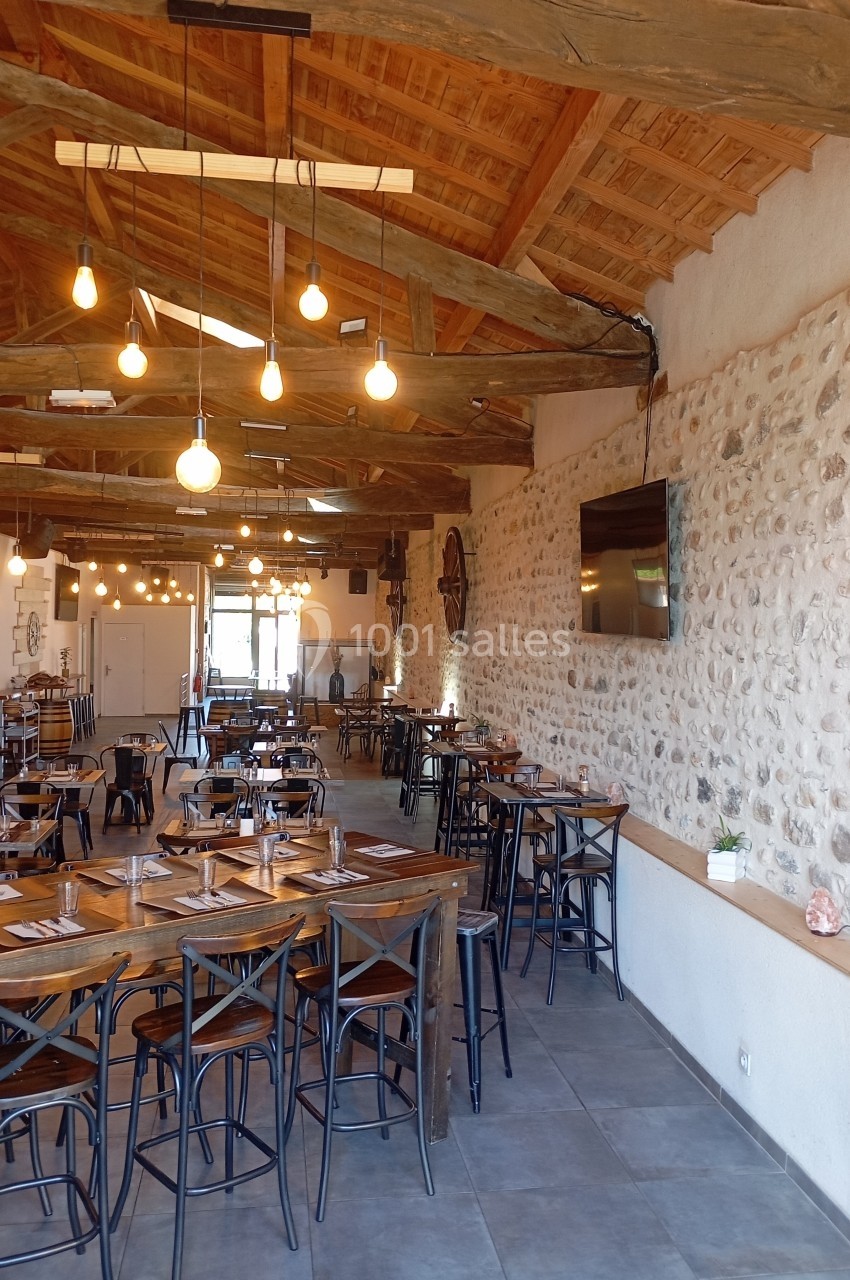 Salle de restaurant lumineuse avec murs en pierre, poutres apparentes et tables en bois dressées.