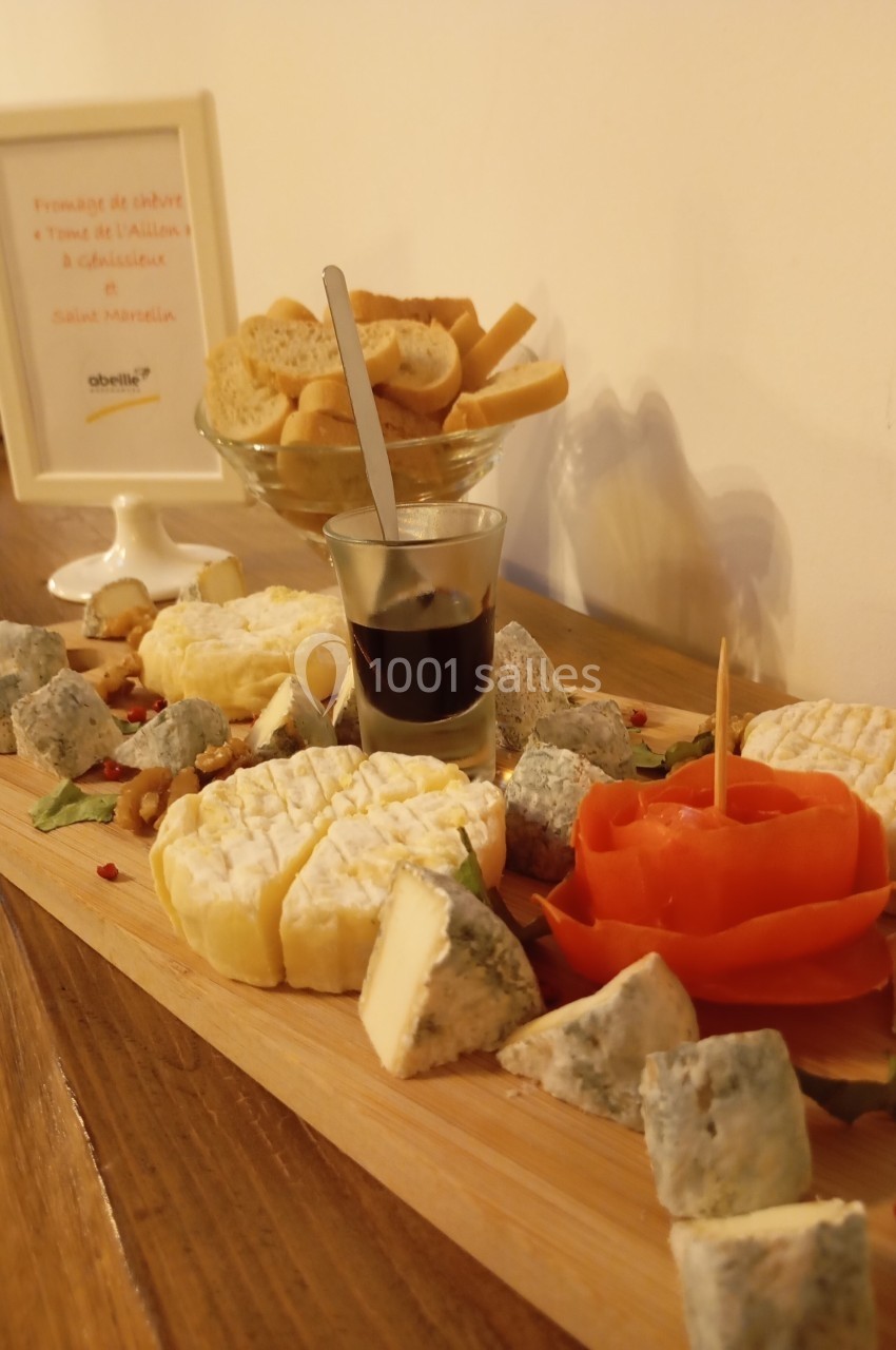 Plateau de fromages variés avec une rose en tomate, un verre de sauce et des tranches de pain en arrière-plan.