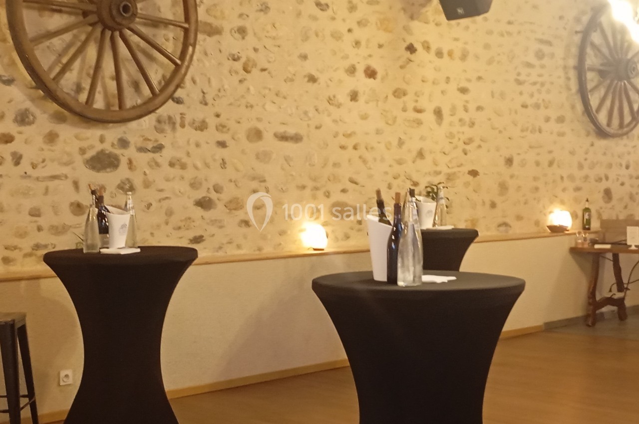 Salle avec murs en pierre, tables hautes noires, seaux à champagne et décorations de roues en bois.