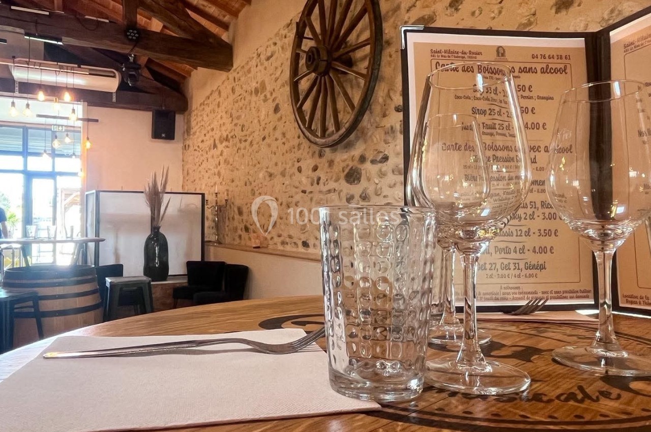 Table dressée avec verre, fourchette et serviette dans un restaurant rustique avec murs en pierre et menu en arrière-plan.