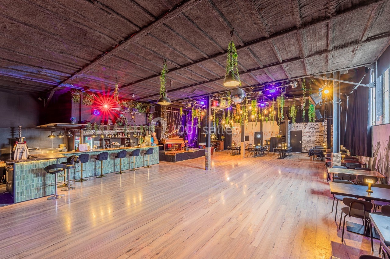 Salle spacieuse avec bar, tables, éclairage coloré et décoration végétale suspendue.