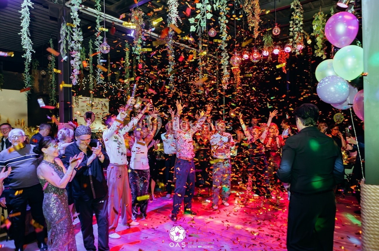 Groupe de personnes célébrant dans une salle décorée, entourées de confettis et de lumières colorées.