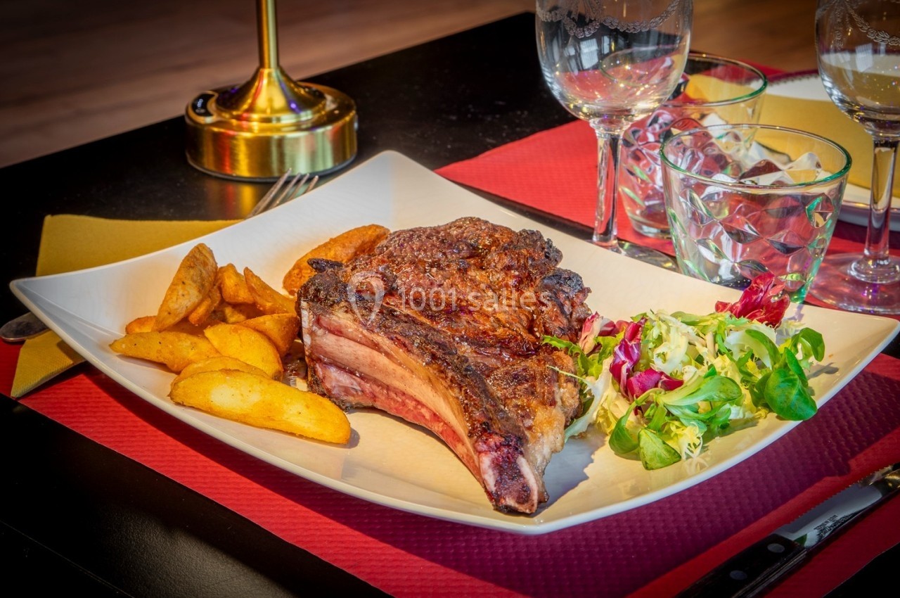 Assiette contenant une côte de bœuf grillée, des pommes de terre rôties et une salade verte, servie sur une table dressée.