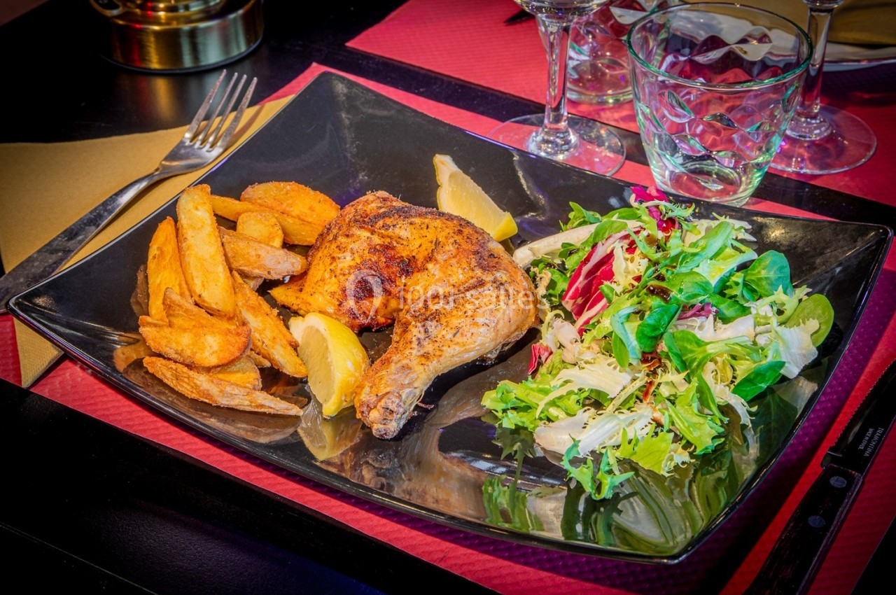 Assiette contenant un morceau de poulet rôti, des pommes de terre rôties et une salade verte sur une table dressée.