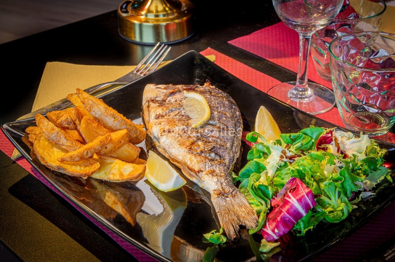 Assiette avec un poisson grillé, des quartiers de pommes de terre, une salade verte et des tranches de citron.