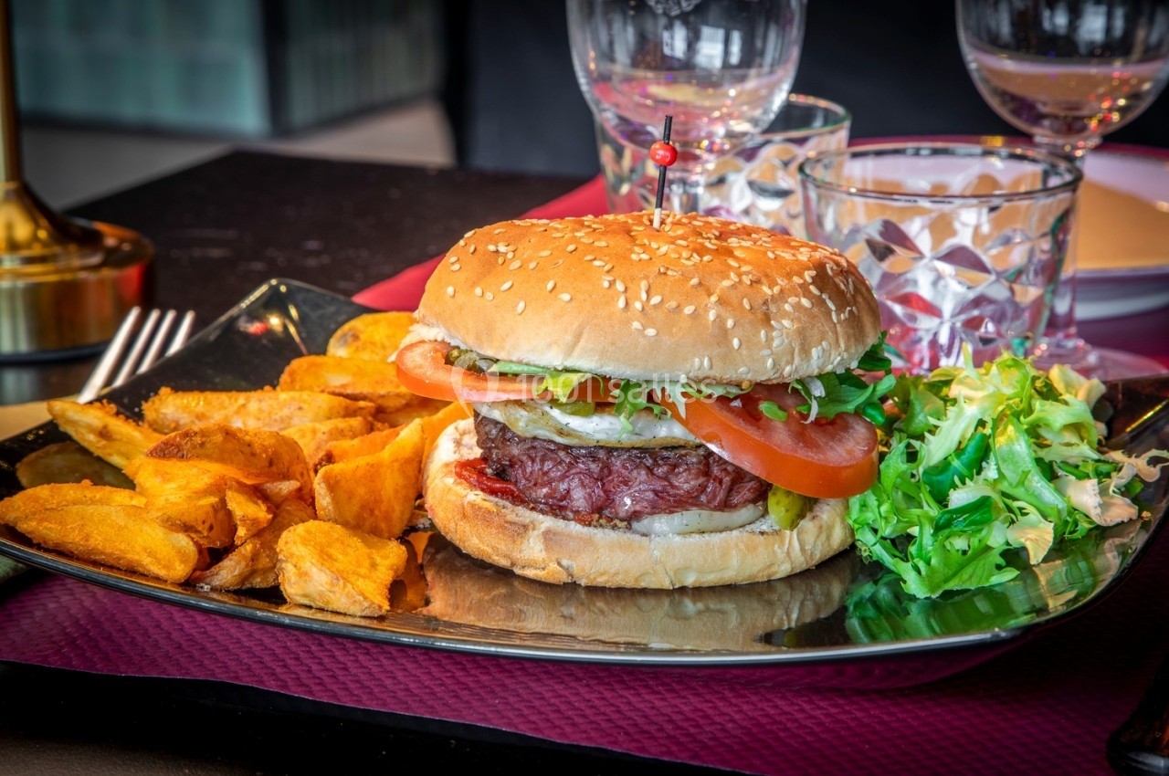 Burger garni de légumes frais accompagné de pommes de terre rôties et d'une salade verte, servi sur une assiette noire.