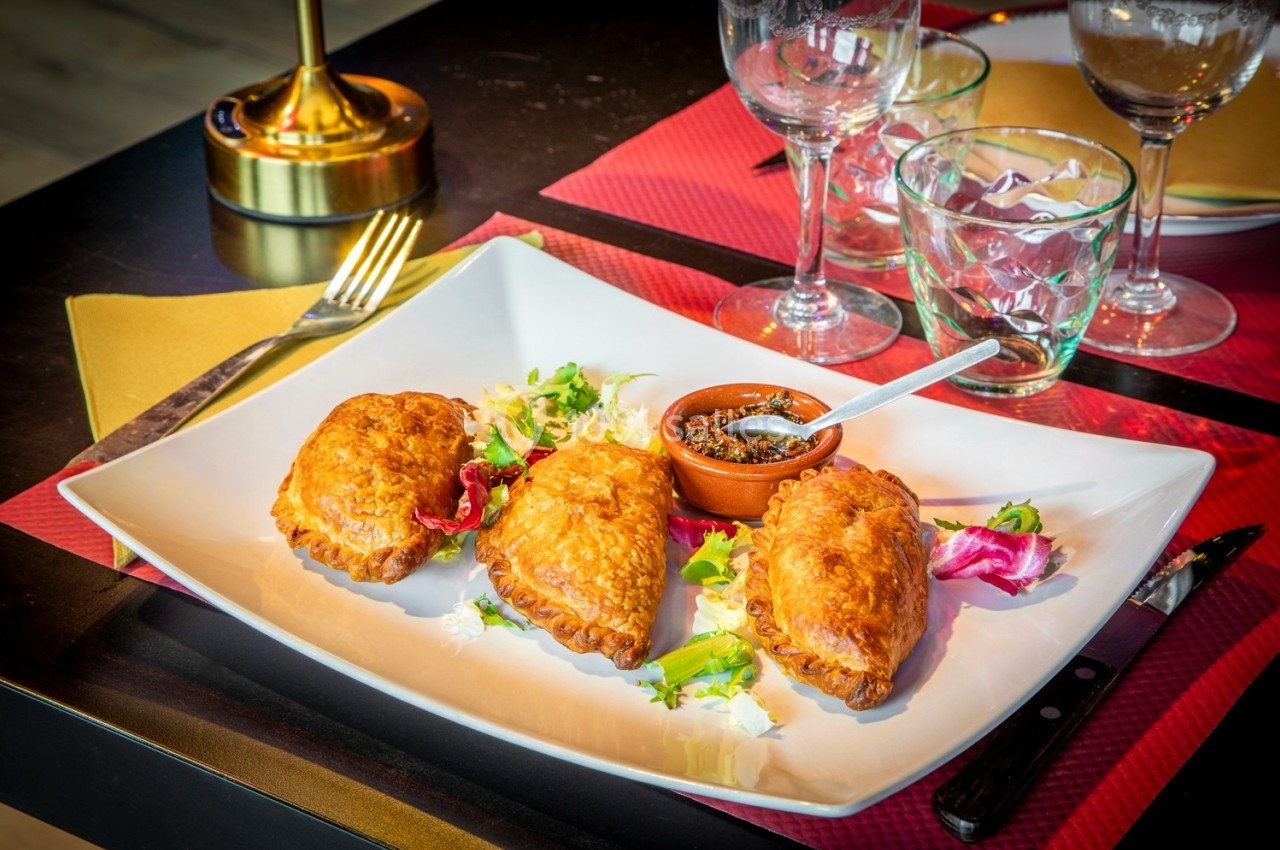 Assiette contenant trois chaussons dorés sur un lit de salade, accompagnés d'une sauce dans un petit ramequin.