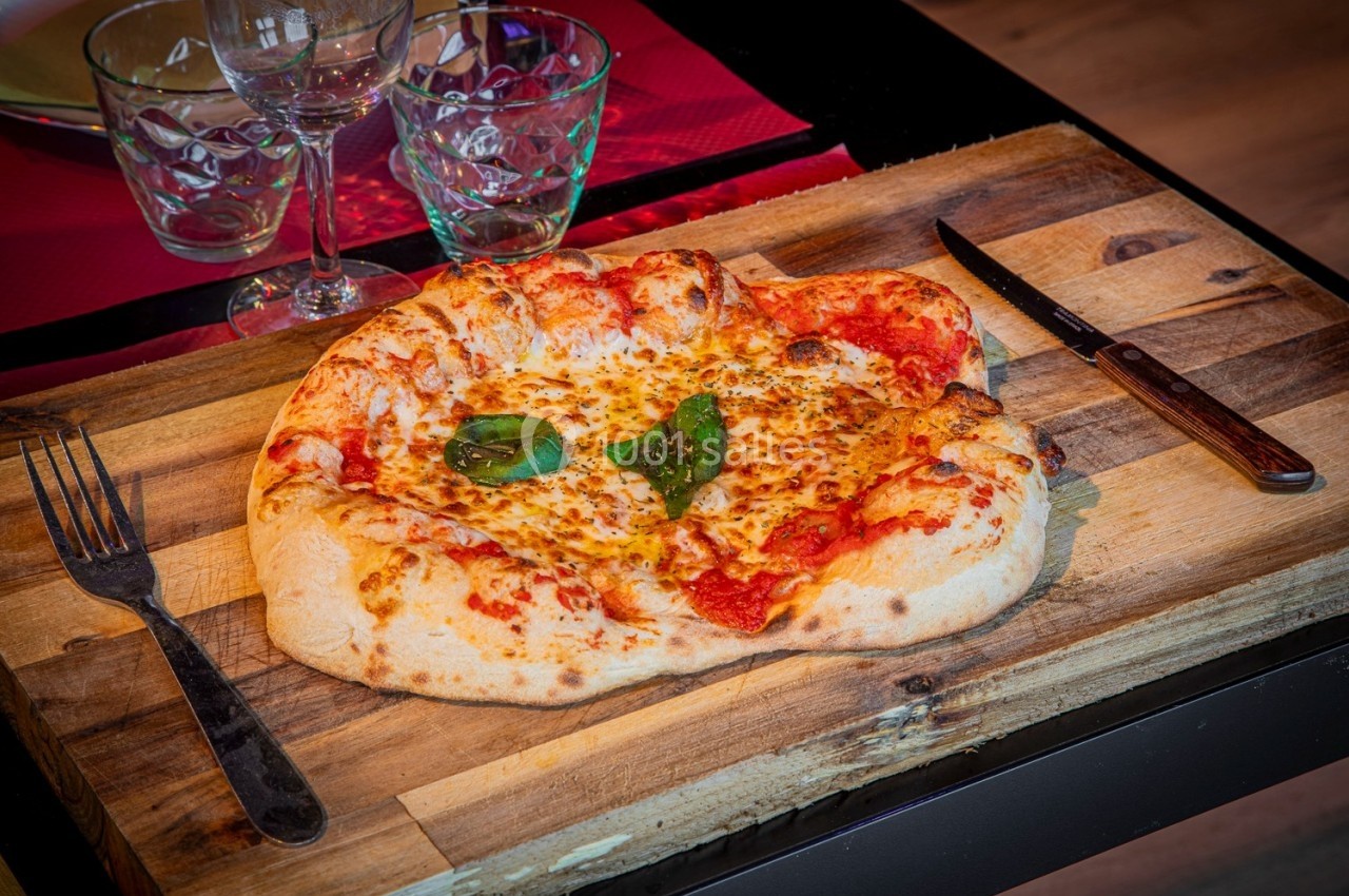 Pizza margherita sur une planche en bois, accompagnée de couverts et de verres sur une table dressée.
