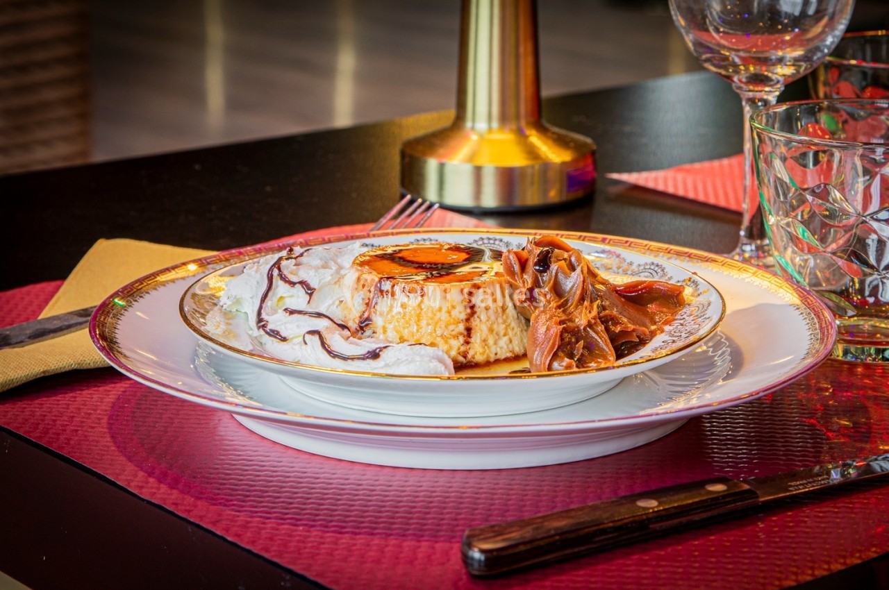 Assiette de flan caramel avec crème fouettée et garniture au chocolat, servie sur une table dressée.