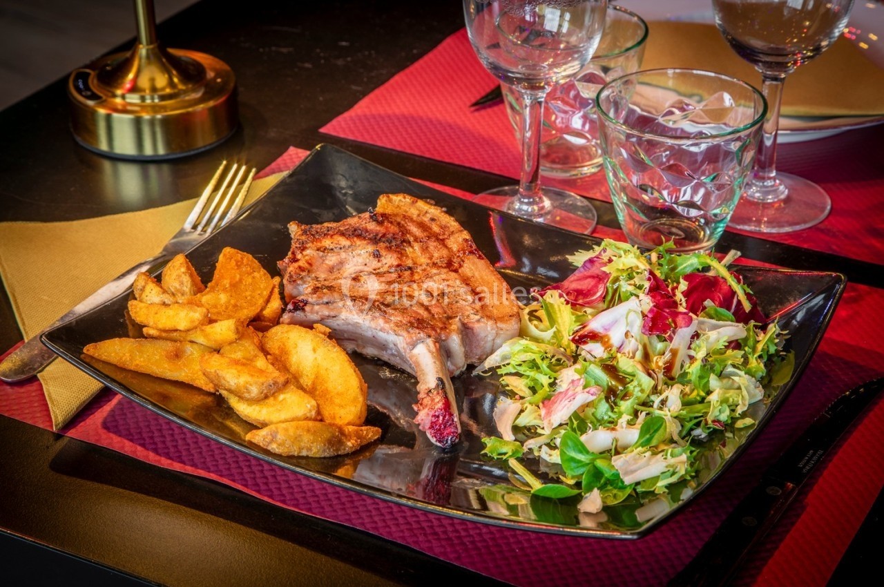 Assiette contenant une côte de porc grillée, des pommes de terre rôties et une salade verte sur une table dressée.