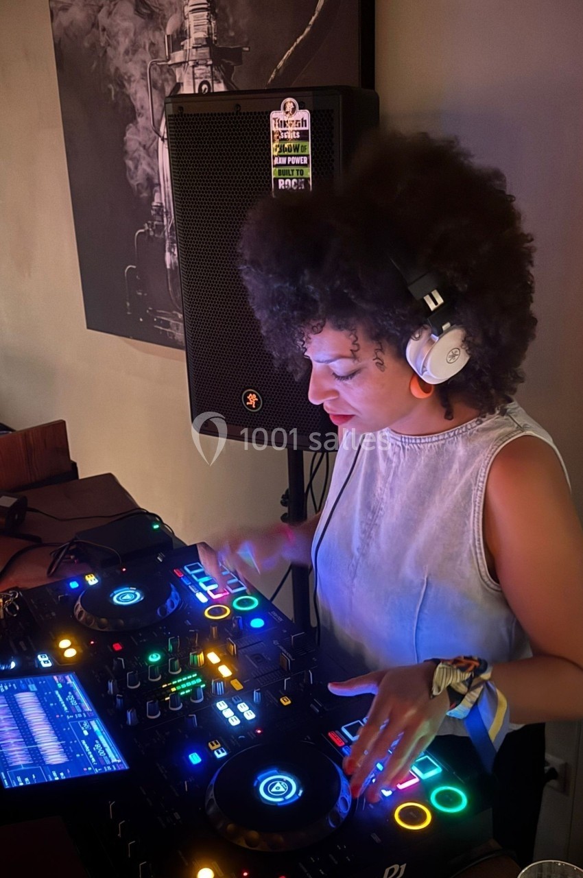 Une DJ concentrée mixe de la musique sur une console éclairée dans une ambiance tamisée.