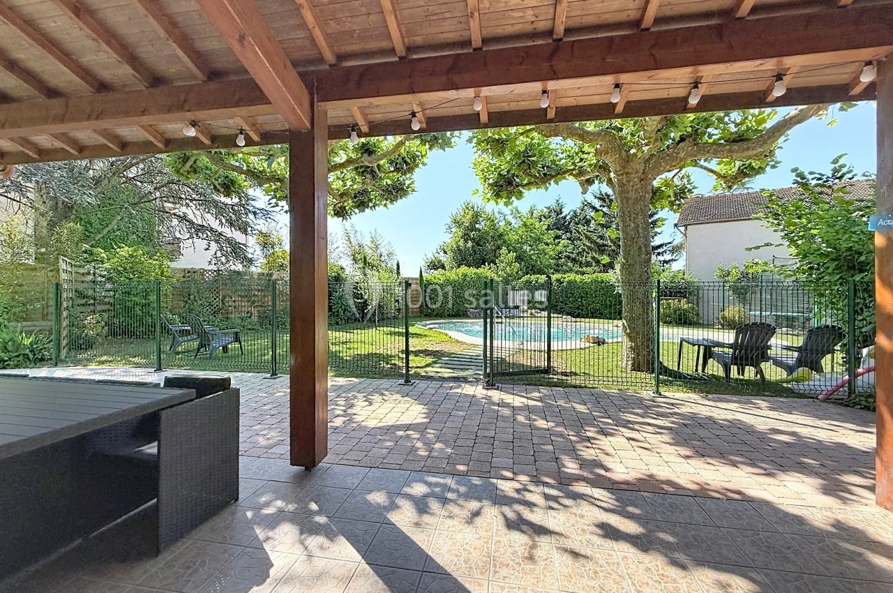 Terrasse couverte avec vue sur un jardin arboré, une piscine clôturée et des chaises disposées à l'extérieur.