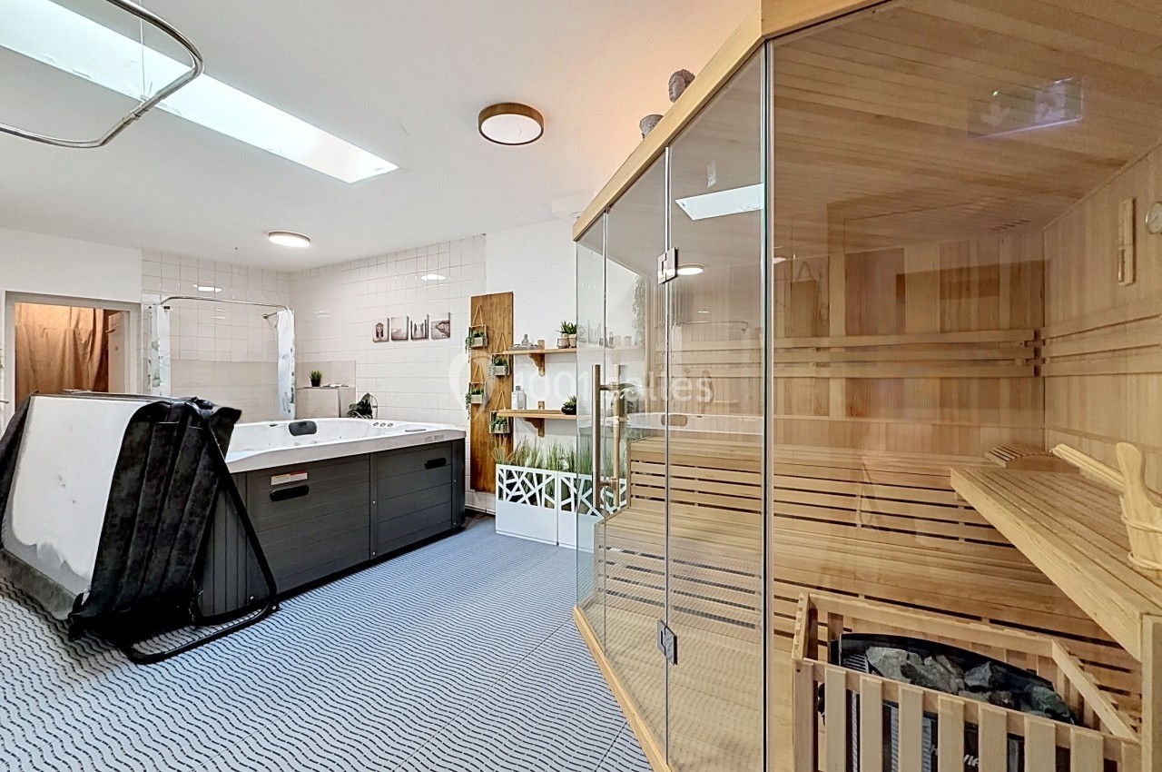 Salle de bien-être avec sauna en bois, baignoire balnéo et décoration naturelle sur un sol à motifs ondulés.