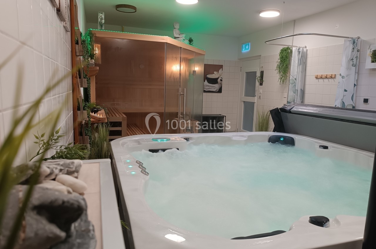 Vue d'un spa intérieur avec jacuzzi allumé au premier plan et sauna en bois en arrière-plan.