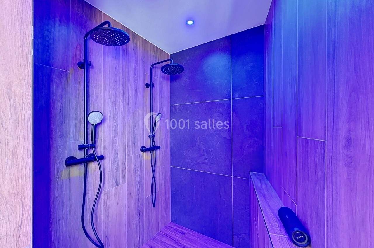Douche double moderne avec parois en bois et carrelage, éclairée par une lumière violette.