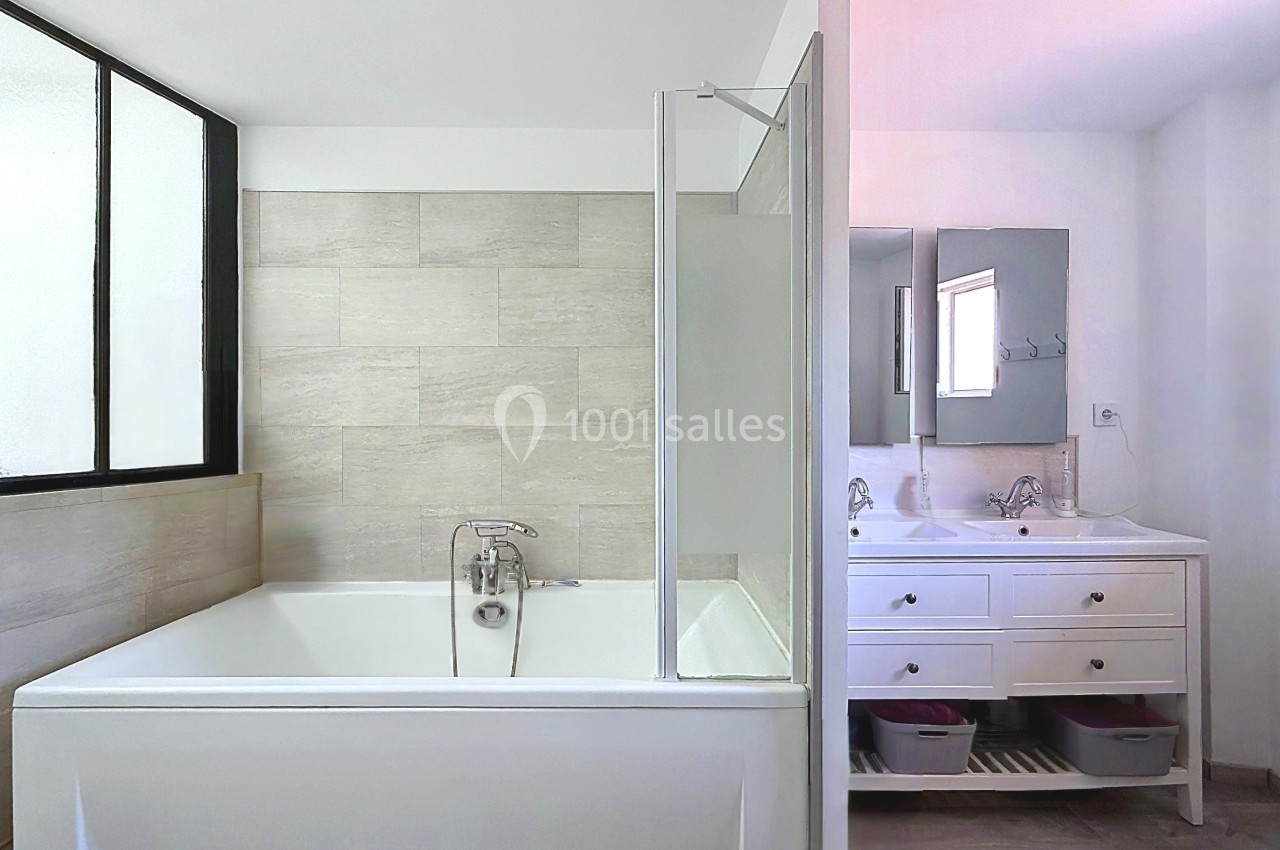 Salle de bain moderne avec baignoire, paroi vitrée, carrelage beige et meuble double vasque blanc.
