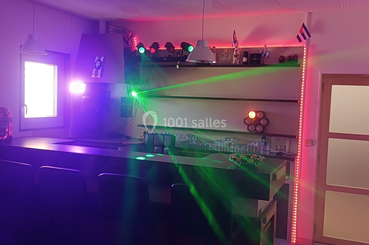 Bar intérieur avec éclairage coloré, lasers verts et rouges, décorations murales et étagères avec verres.