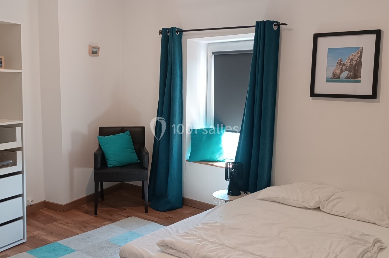 Chambre lumineuse avec lit simple, étagère, chaise, rideaux bleus et tableau décoratif au mur.