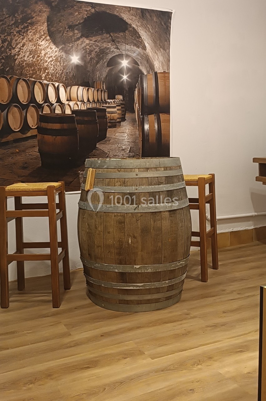 Tonneau en bois utilisé comme table, entouré de tabourets, avec une photo de cave à vin en arrière-plan.