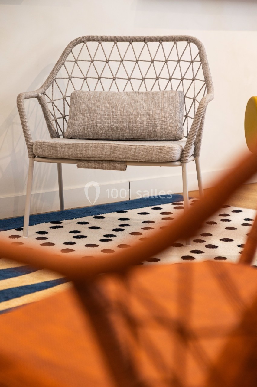 Chaise en corde tressée beige avec coussin gris, posée sur un tapis à motifs noirs et blancs.