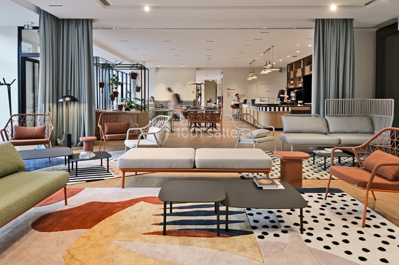 Espace lounge moderne avec canapés, fauteuils et tables basses, décoré de tapis colorés et plantes en arrière-plan.