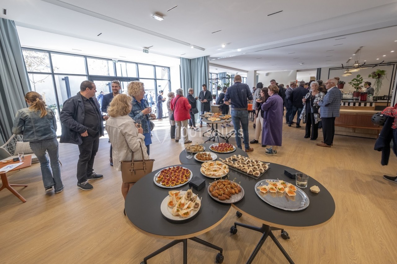 Des personnes discutent dans une salle lumineuse avec des tables garnies de plats variés au premier plan.