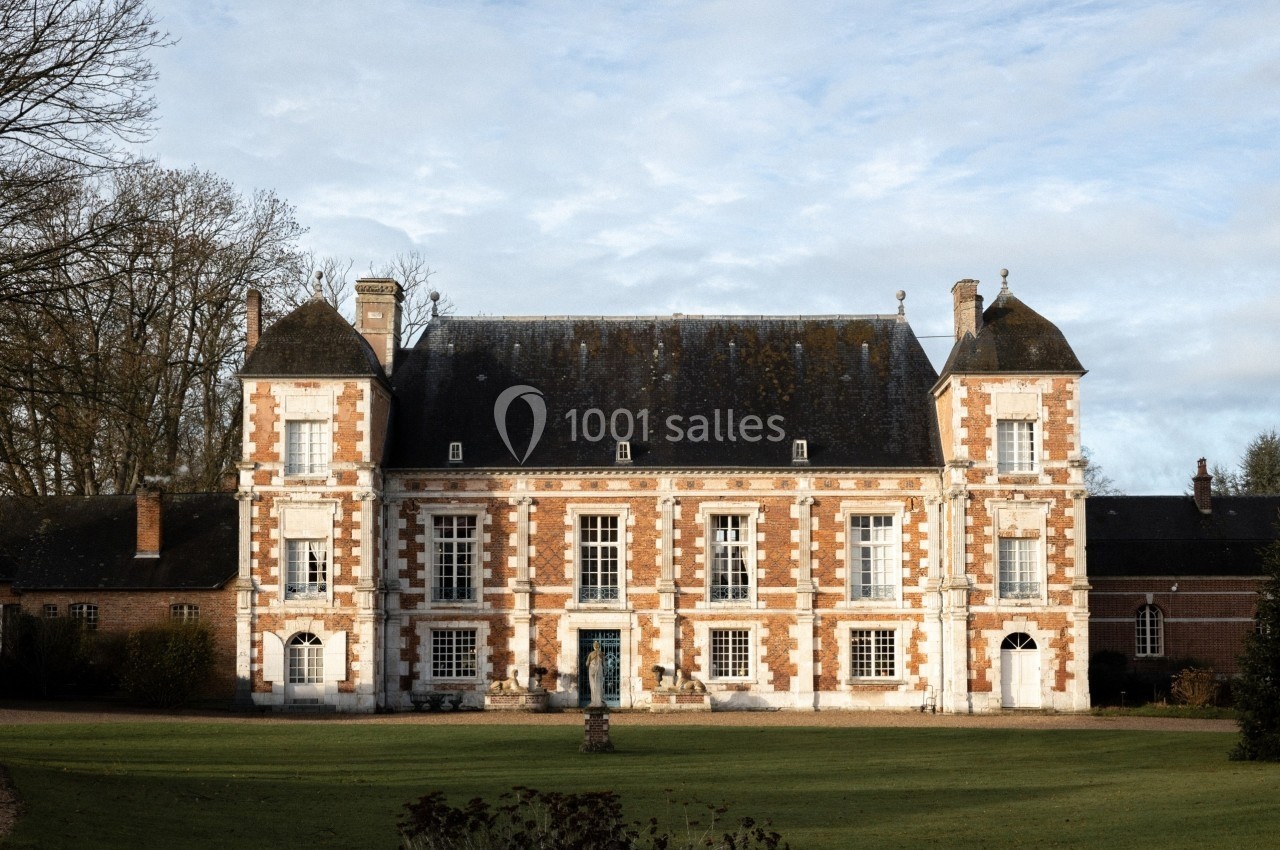 Façade d'un château en briques rouges et blanches entouré d'une pelouse et d'arbres en arrière-plan.