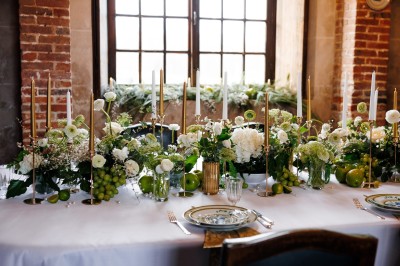 Des mariés et leurs invités trinquent autour d'une table décorée de fleurs et de bougies dans une salle rustique.