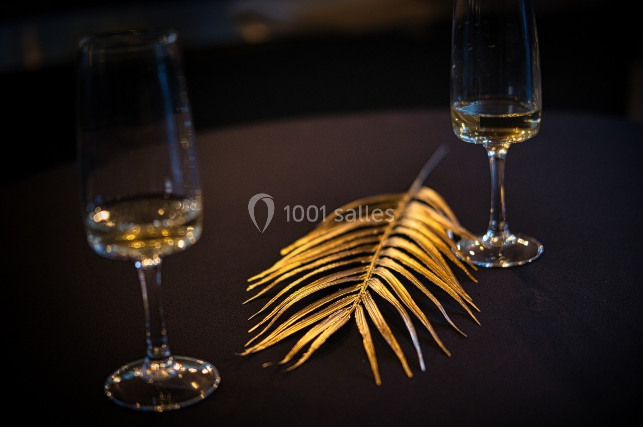 Deux verres à pied partiellement remplis entourent une feuille dorée posée sur une table sombre.