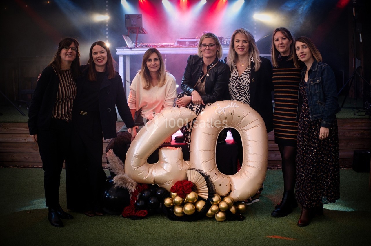 Sept femmes posant devant une décoration marquant ’40’, avec des ballons et un éclairage festif en arrière-plan.